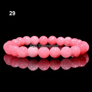 Puede incluir: Una pulsera de cuentas rosas con un acabado brillante. La pulsera está hecha de cuentas redondas y pulidas. El texto "29" está en la esquina superior izquierda y "A2Z Cabochon" en la esquina inferior derecha.