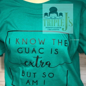 Puede incluir: Una camiseta verde turquesa con un gráfico cuadrado negro que dice "Sé que el guacamole es extra, pero yo también". El gráfico está rodeado por un borde negro. La camiseta tiene cuello redondo y mangas cortas. La camiseta tiene un logotipo en la esquina superior derecha que dice "Triple J's Personalized Creations".