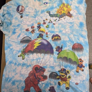 May include: A tie-dye blue t-shirt with a Grateful Dead graphic. The graphic features a sun with a face, bears with parachutes, and the text "Grateful Dead".
