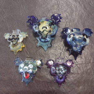 May include: Five glass pendants with cartoon bear faces. The bears have different colored glass and facial expressions. The pendants are all in the shape of a bear head with a dripping effect.