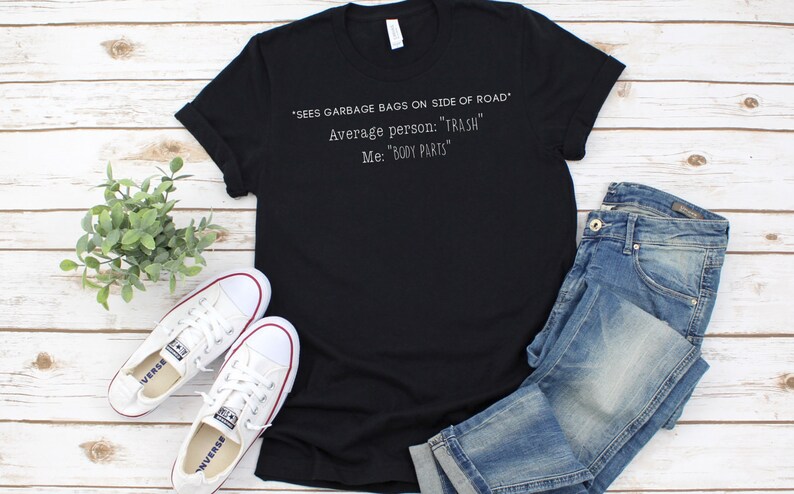 May include: Black t-shirt with white text that reads "*SEES GARBAGE BAGS ON SIDE OF ROAD* Average person: "TRASH" Me: "BODY PARTS"