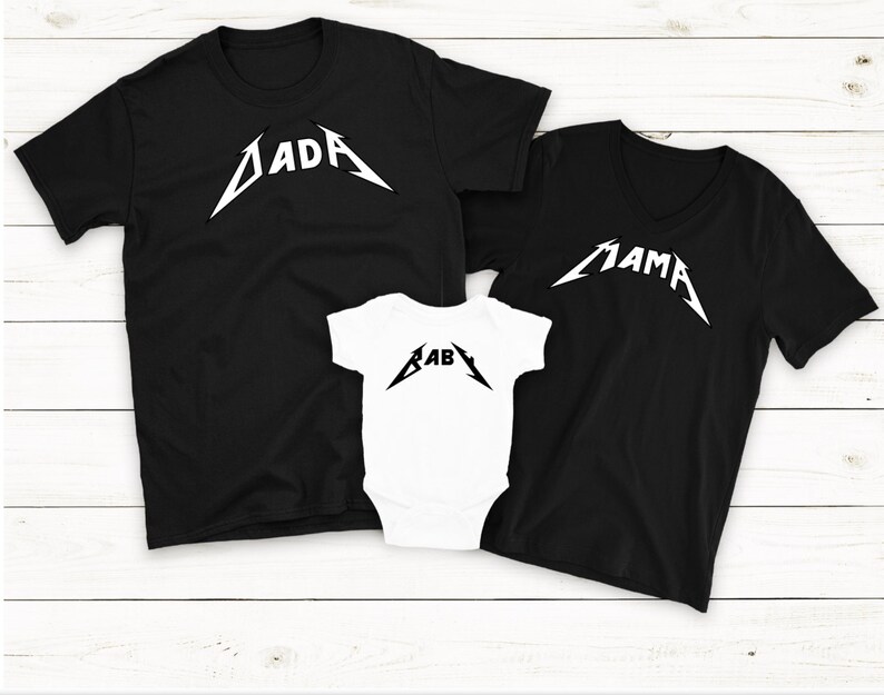 Op de afbeelding: Drie zwarte T-shirts met witte tekst in een metalband-stijl lettertype. De shirts zeggen "Dada", "Mama" en "Baby".