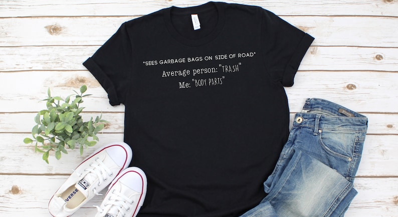 May include: Black t-shirt with white text that reads: "SEES GARBAGE BAGS ON SIDE OF ROAD" Average person: "TRASH" Me: "BODY PARTS"