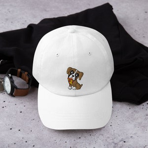 May include: White baseball cap with a curved brim. The cap features an embroidered cartoon dog with brown and white fur, holding a slice of pizza. The dog is wearing a red collar. The cap is a classic, casual accessory.