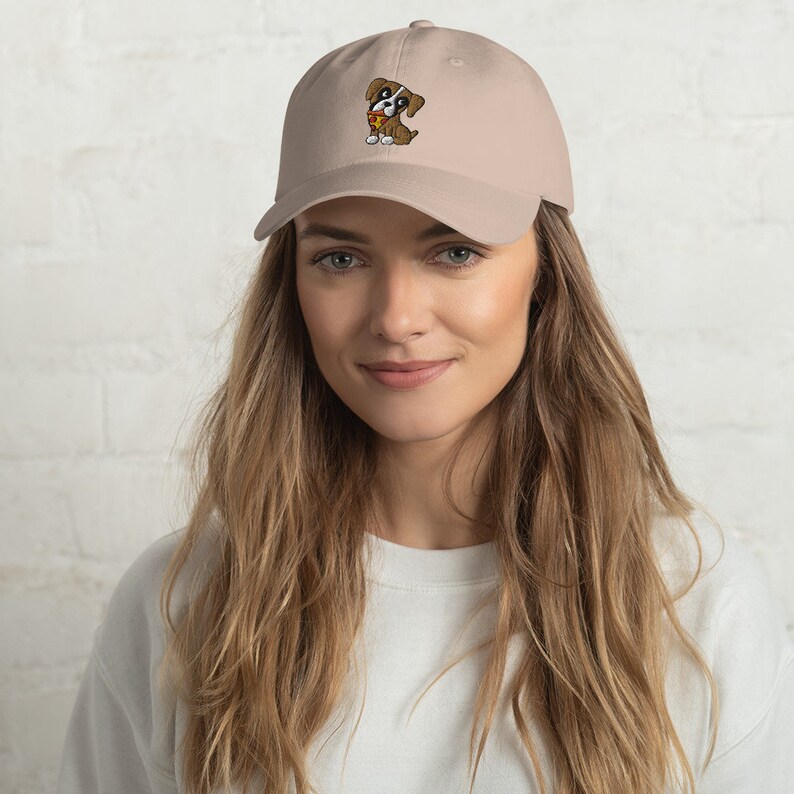 May include: A beige baseball cap featuring an embroidered cartoon puppy with brown, white, and yellow accents. The cap has a curved brim and a classic six-panel design, suitable for casual wear.