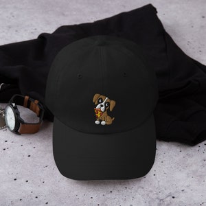 May include: Black baseball cap with an embroidered cartoon dog holding a slice of pizza. The dog is brown and white with a red collar. The cap is made of a soft material and has a curved brim.