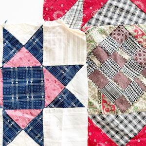 May include: Two fabric quilt blocks featuring patchwork designs. One block displays a central star pattern in navy blue, pink, and white. The second block features a grid of small squares in black, white, brown, and green, bordered by red fabric.