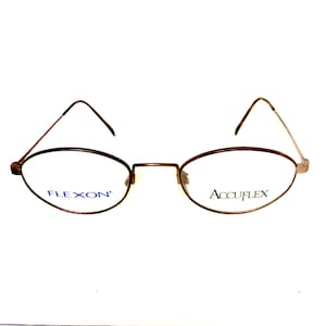 May include: Brown metal oval-shaped eyeglasses with a silver bridge. The left lens has the word "FLEXON" printed in blue and the right lens has the word "ACCUFLEX" printed in blue.