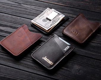May include: Four leather card holders with a money clip. The card holders are brown, black, and dark brown. The money clip is silver. The card holders have the names "James", "JM", and "VISA" embossed on them.