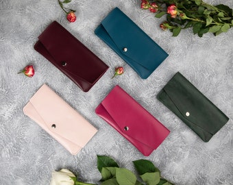 May include: Five leather wallets in different colors: pink, burgundy, teal, green, and magenta. The wallets are laid out on a gray textured surface.
