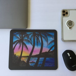 Pode incluir: Tapete de rato retangular preto com uma cena colorida de p&ocirc;r do sol na ilha com palmeiras, oceano e um c&eacute;u vibrante. O tapete do rato est&aacute; ao lado de um laptop, um smartphone e um rato sem fios preto.