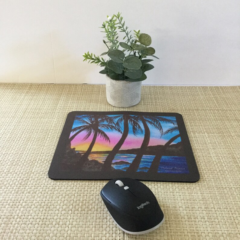 Pode incluir: Tapete de rato retangular preto com uma cena de p&ocirc;r do sol colorida com palmeiras, oceano e c&eacute;u em tons de azul, rosa e amarelo. Um rato de computador preto est&aacute; posicionado abaixo. Uma pequena planta em vaso est&aacute; no fundo.