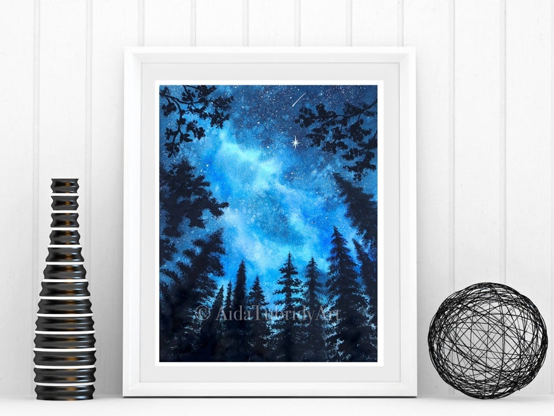 May include: A framed watercolor painting of a night sky with a bright blue and white galaxy. Silhouetted trees frame the bottom and sides of the image. The artist's signature, "AidaTrifidyArt", is visible in the lower right corner.