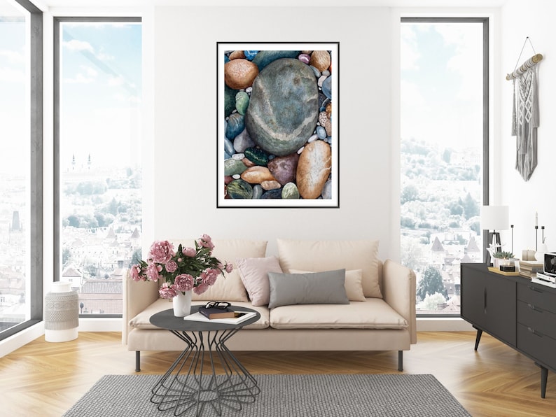May include: A framed art print featuring a close-up of colorful river rocks. The rocks vary in size and color, with shades of blue, green, brown, and gray. The artwork is displayed in a living room setting with a neutral-toned sofa and a city view.
