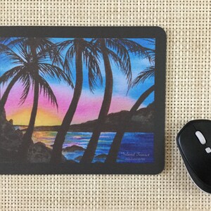 Pode incluir: Tapete de rato retangular preto com uma pintura em aquarela de um p&ocirc;r do sol tropical com palmeiras. A obra de arte inclui tons de rosa, azul e amarelo. O texto "Island Sunset" &eacute; vis&iacute;vel. Um rato sem fios preto est&aacute; ao lado.