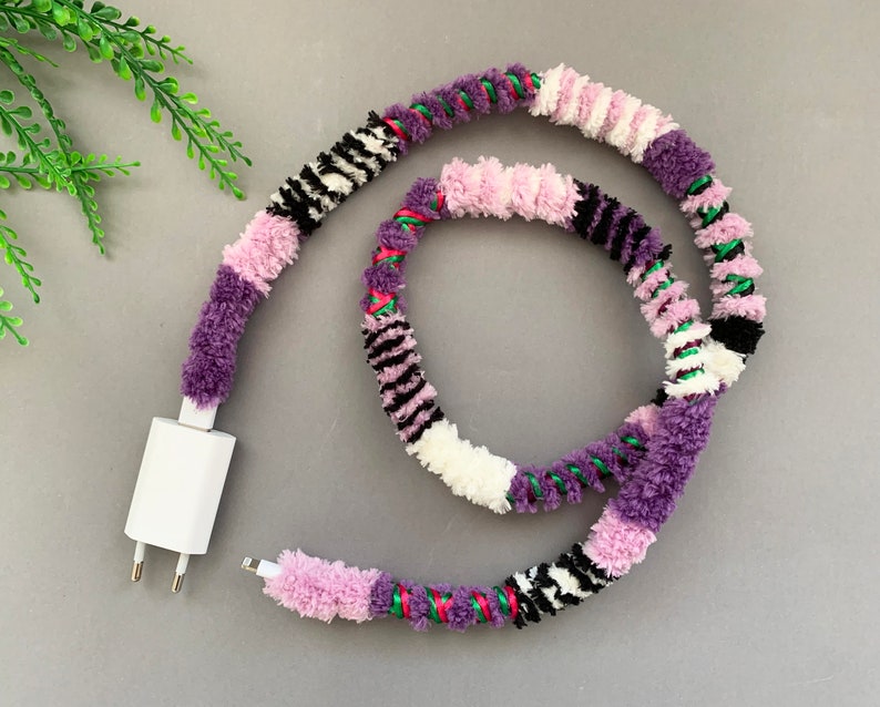 May include: A white phone charger cord wrapped in a colorful yarn with purple, pink, white, black, and green stripes.