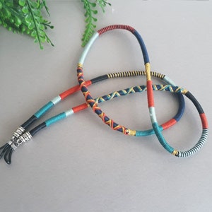 May include: A colorful braided eyeglass chain with black cord ends and silver metal clasps. The chain is made of blue, red, green, and gold threads.