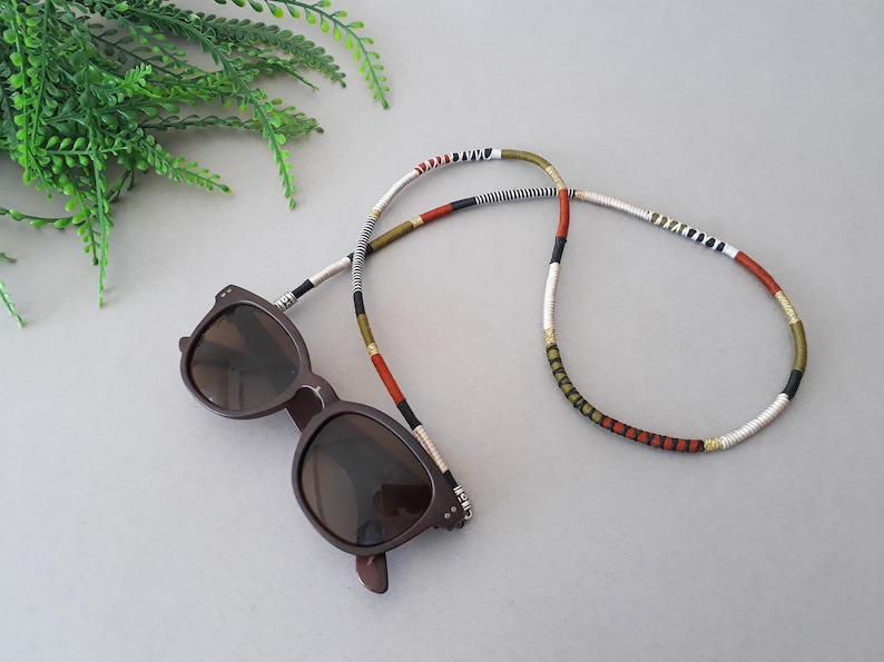 May include: A pair of brown sunglasses with a colorful beaded eyeglass chain. The chain is made of white, black, red, and green beads.