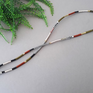 May include: A pair of black and white striped eyeglass retainers with red, gold, and green accents. The retainers are made of woven cord and have silver metal ends.