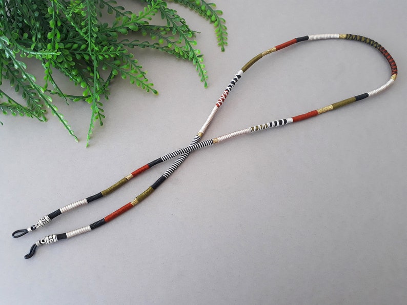 May include: A pair of black and white striped eyeglass retainers with red, gold, and green accents. The retainers are made of woven cord and have silver metal ends.