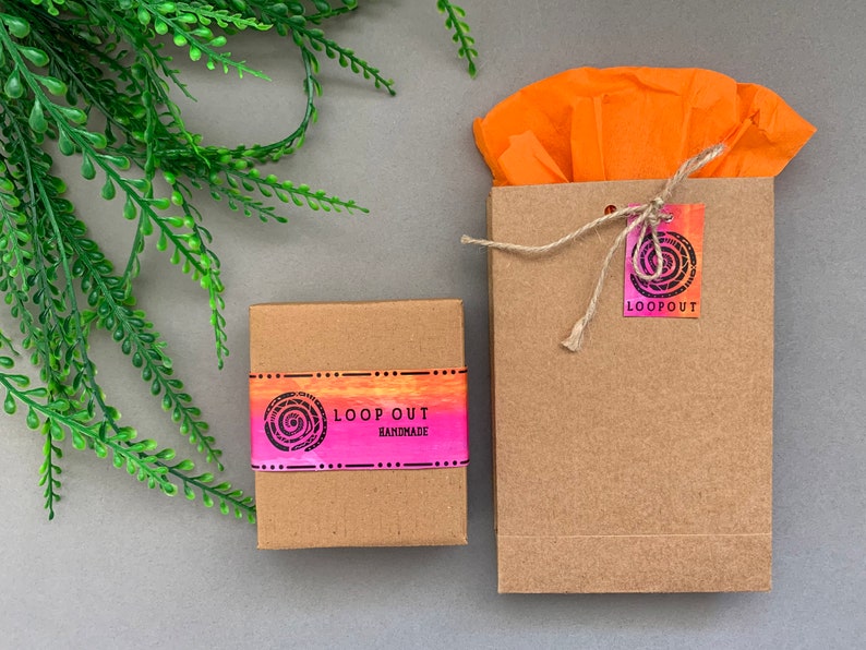 May include: Two brown cardboard boxes with a pink and orange graphic design. The smaller box has the text "LOOP OUT HANDMADE" on it. The larger box has a tag with the text "LOOP OUT" on it.