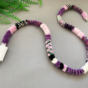 May include: A white phone charger cord wrapped in a colorful yarn with purple, pink, white, black, and green stripes.