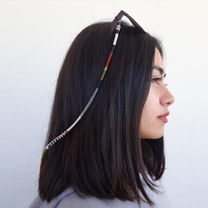 May include: A close-up of a person wearing a beaded glasses chain with black, white, red, and green beads. The chain is attached to the glasses and hangs down the side of the person's head.