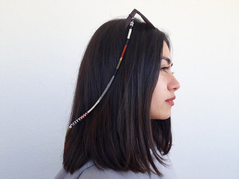 May include: A close-up of a person wearing a beaded glasses chain with black, white, red, and green beads. The chain is attached to the glasses and hangs down the side of the person's head.
