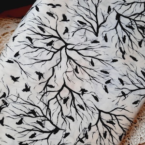 Könnte beinhalten: Weißer Stoff mit einem Muster aus schwarzen Ästen und Vögeln. Das Design zeigt silhouettierte Vögel, die auf den Ästen sitzen und um sie herumfliegen. Der Stoff ist gefaltet und zeigt die sich wiederholende Natur des Musters.