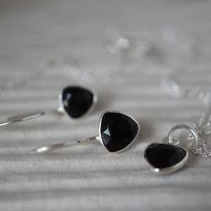 Puede incluir: Un conjunto de collar y pendientes de plata con colgantes de piedras preciosas negras. Los colgantes son de forma triangular.