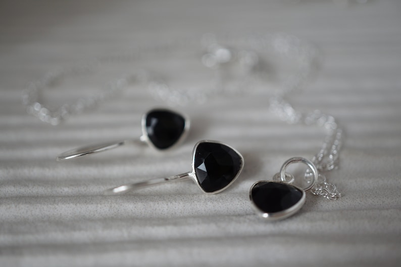 Puede incluir: Un conjunto de collar y pendientes de plata con colgantes de piedras preciosas negras. Los colgantes son de forma triangular.