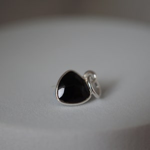 Puede incluir: Un amuleto de plata con una piedra preciosa triangular negra.