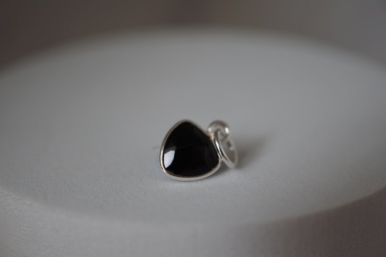 Puede incluir: Un amuleto de plata con una piedra preciosa triangular negra.