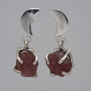 Puede incluir: Un par de pendientes de plata con un diseño de media luna y una piedra preciosa rosa que cuelga de cada uno.