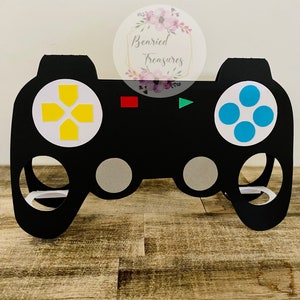 May include: Black cardboard video game controller cutout with yellow and blue buttons. The controller is designed to hold treats or small gifts.