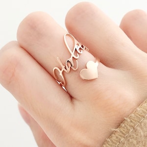 Op de afbeelding: Een gouden ring met de naam "Sabrina" in cursief schrift. De ring heeft een klein hartje aan de zijkant.