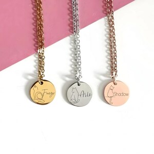 May include: Three necklaces with round metal pendants hanging from delicate chains. The left pendant is gold with a cat outline and the name Fuego. The center pendant is silver with a cat outline and the name Arlo. The right pendant is rose gold with a cat outline and the name Shadow.