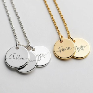 May include: Two necklaces with personalized name tags. The first necklace is silver and has three round tags with the names "Peter", "Olivia" engraved on them. The second necklace is gold and has two round tags with the names "Fiona" and "Aoife" engraved on them.