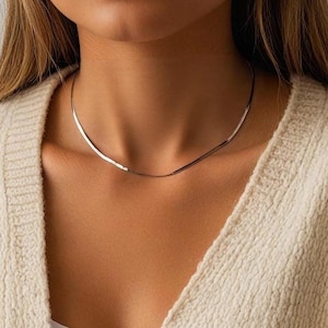 以下が含まれることがあります： クリーム色のカーディガンを着た女性が、シルバーのチェーンネックレスをしている