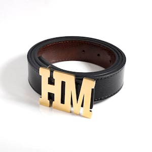 A custom gold belt buckle crafted with three custom letters or initials