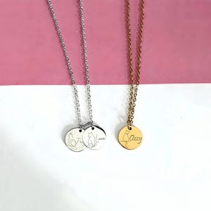 May include: Two silver-toned necklaces with circular pendants featuring engraved cat outlines and the names Luna and Fugi, alongside one gold-toned necklace with a circular pendant featuring an engraved cat outline and the name Ozzy.