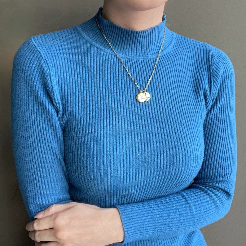 May include: A bright blue ribbed mock neck long-sleeve sweater paired with a gold-toned chain necklace featuring two small, round, engraved pendants that hang centrally against the textured fabric of the knit garment.