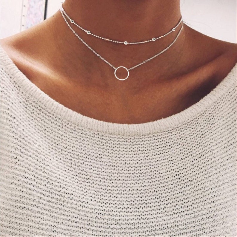 A short necklace that is made in two layers. The upper strand is a dainty beads chain and the lower strand is a cable chain, with a minimalist ring hung in the middle. It can be worn as a choker, offering a delicate style.