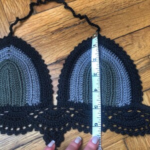 May include: A black, gray, and green crocheted halter top with a scalloped bottom edge. The top is being measured with a tape measure that shows 6 inches.