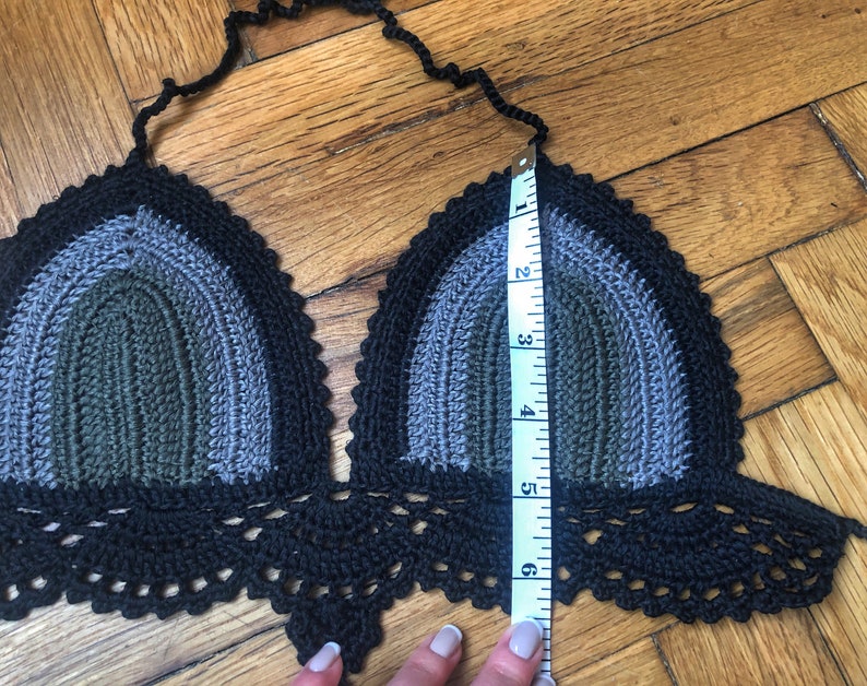 May include: A black, gray, and green crocheted halter top with a scalloped bottom edge. The top is being measured with a tape measure that shows 6 inches.
