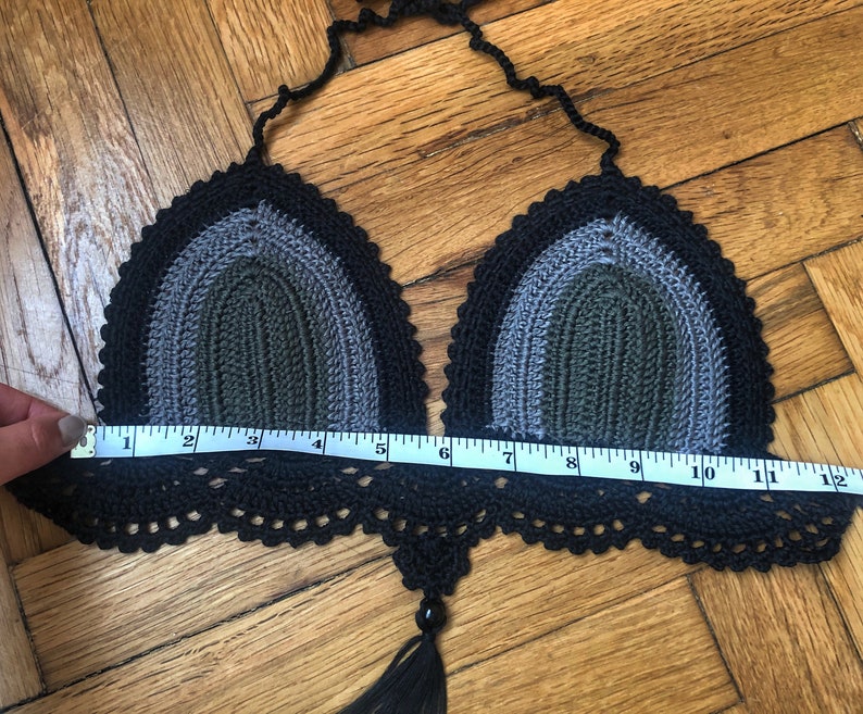 May include: Black, gray, and green crochet bikini top with a tassel. The top measures 10 inches across.