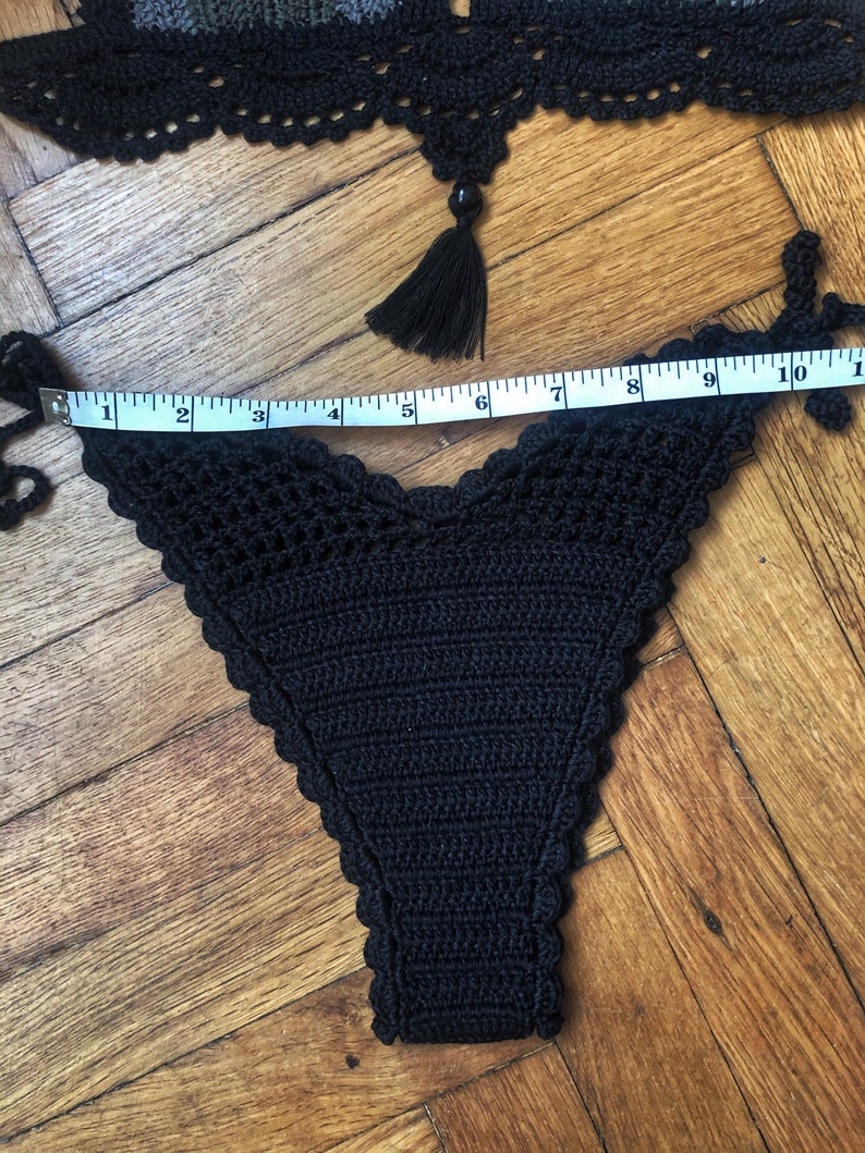 May include: Black crocheted bikini bottom with a scalloped edge. The bottom is measured with a tape measure, showing a length of 10 inches.