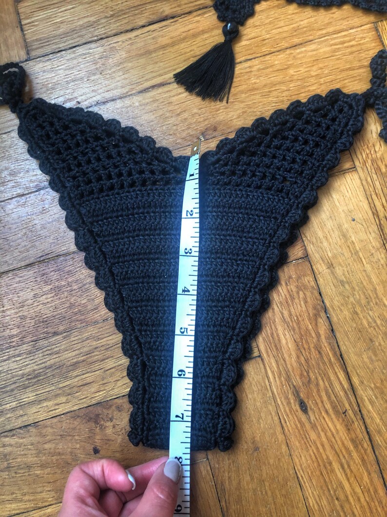 May include: Black crocheted bikini bottom with a scalloped edge, measured with a tape measure to be 7 inches long.