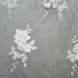 May include: White floral lace fabric with delicate 3D flowers and pearl accents. The fabric is sheer and lightweight, perfect for adding a touch of elegance to any project.