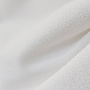 May include: Close-up of a white fabric with a textured surface. The fabric is soft and smooth, with a subtle sheen.